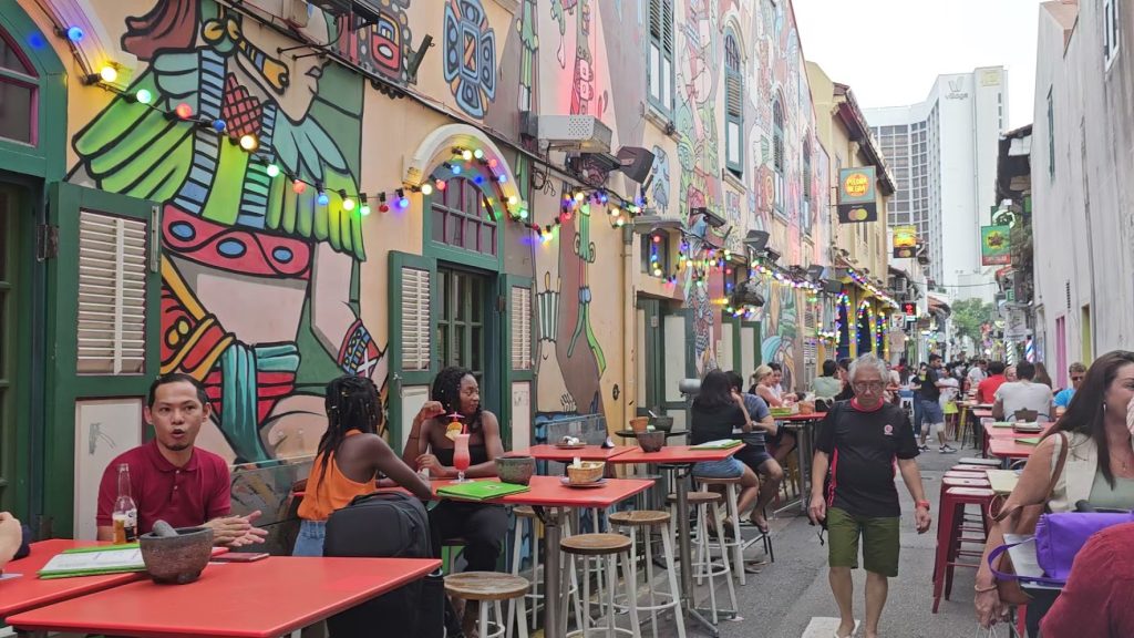 VICOLO COLORATO PIENO DI RISTORANTI E PERSONE CHE SI RILASSANO BEVENDO E MANGIANDO IN HAJI LANE