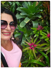 IMMAGINE DELL'AUTRICE IN UN ANGOLO DEI GIARDINI BOTANICI ACCANTO AD UNA PIANTA EQUATORIALE CON UN FIORE FUXIA ROSA